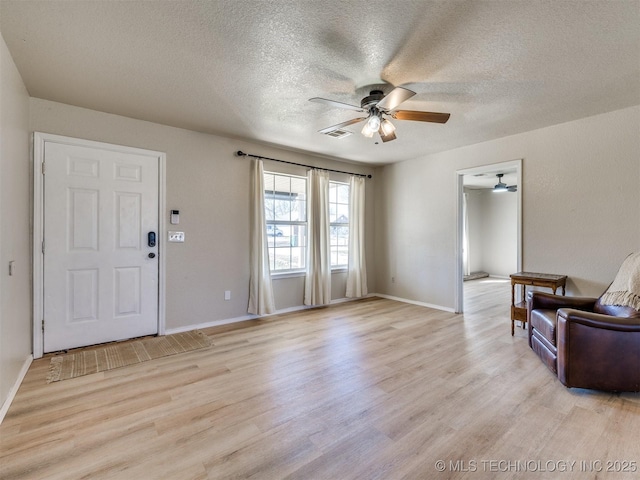 living area featuring visible vents, light wood-style floors, ceiling fan, and a textured ceiling