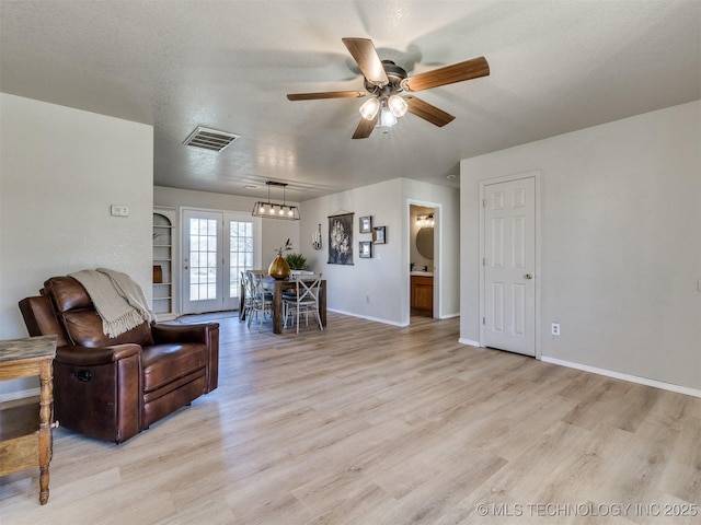 living room featuring visible vents, light wood-style flooring, a textured ceiling, baseboards, and ceiling fan