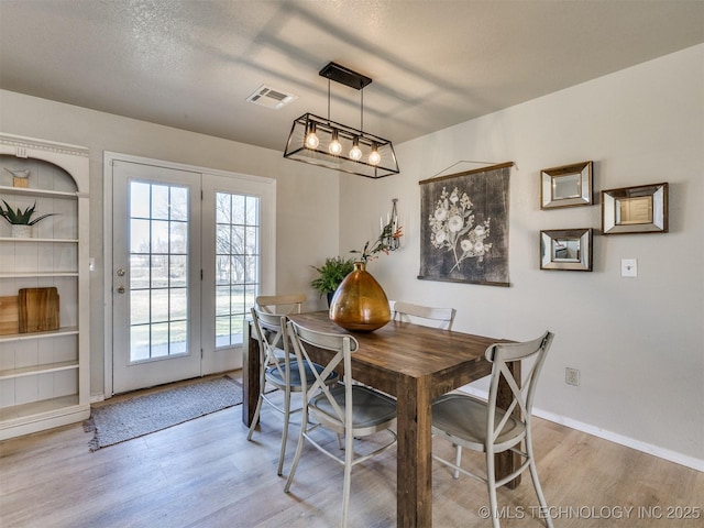 dining space with a textured ceiling, light wood-style floors, visible vents, and baseboards