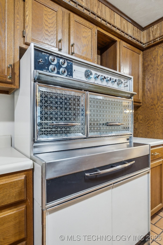 kitchen with brown cabinetry, light countertops, and wallpapered walls