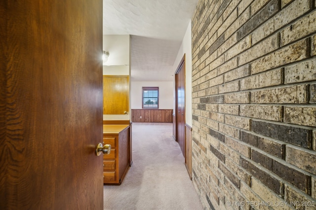 corridor featuring a wainscoted wall, brick wall, and carpet