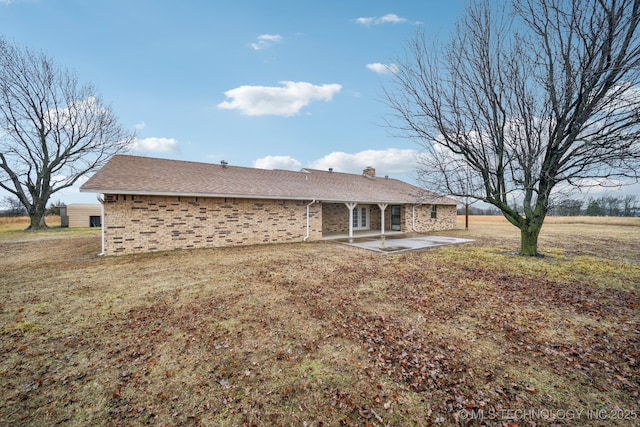 back of property with brick siding, a shingled roof, a chimney, and a patio