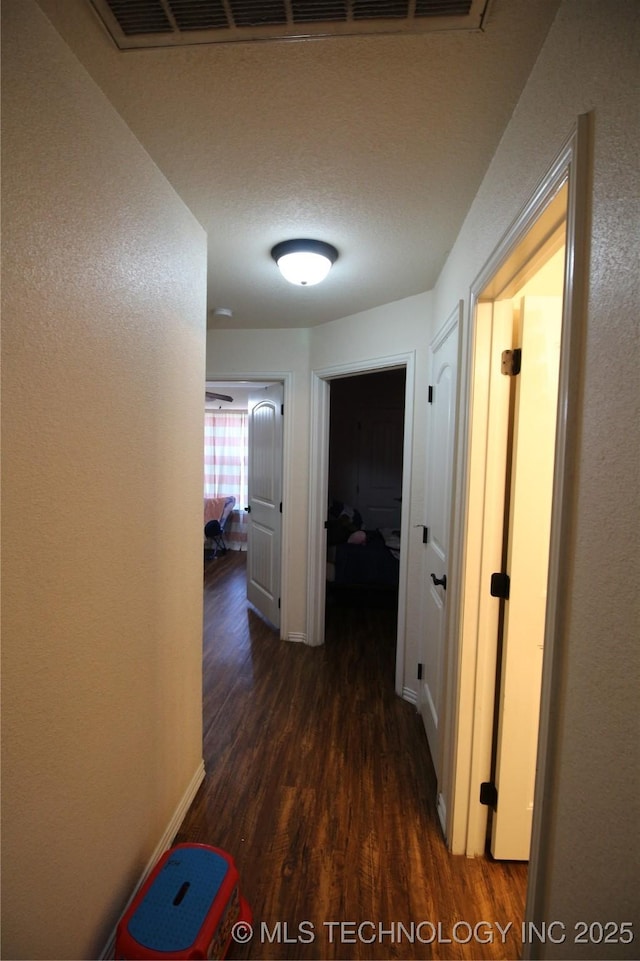 hall with a textured ceiling, a textured wall, wood finished floors, and baseboards