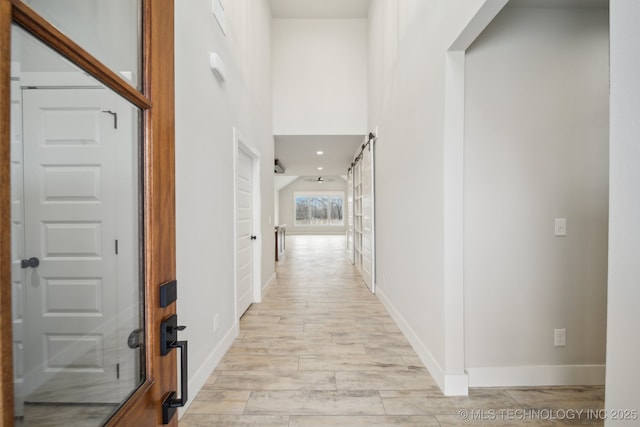 hallway featuring a towering ceiling, light wood-style floors, and baseboards