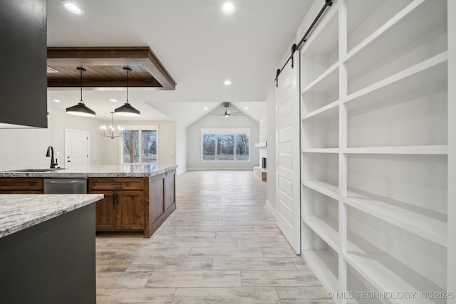 kitchen featuring a barn door, light stone counters, wood tiled floor, stainless steel dishwasher, and a sink