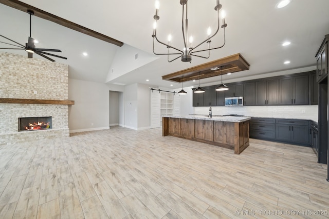 kitchen featuring a fireplace, a raised ceiling, stainless steel microwave, open floor plan, and ceiling fan