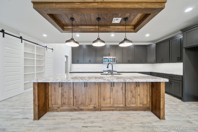 kitchen featuring a tray ceiling, a barn door, stainless steel microwave, and visible vents