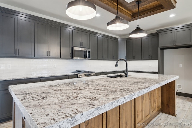 kitchen featuring stainless steel microwave, stove, a tray ceiling, light wood-style floors, and a sink