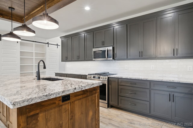 kitchen featuring appliances with stainless steel finishes, tasteful backsplash, a sink, and a barn door