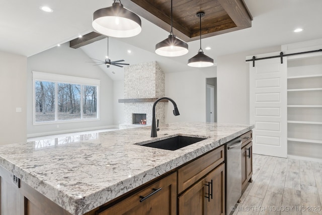 kitchen featuring a barn door, dishwasher, a ceiling fan, a stone fireplace, and a sink