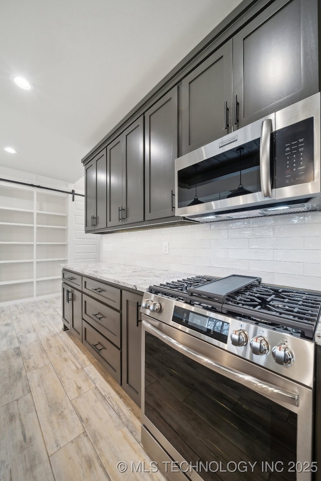 kitchen featuring a barn door, light stone counters, stainless steel appliances, light wood-type flooring, and tasteful backsplash