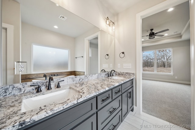 bathroom featuring a tray ceiling, visible vents, a sink, and double vanity