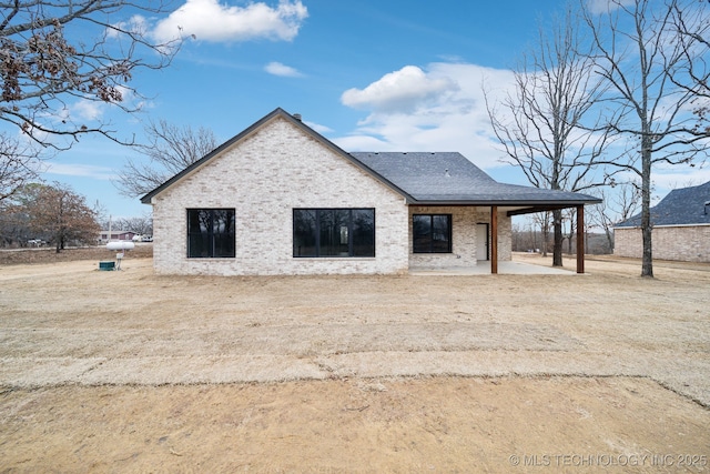 back of property with a shingled roof, a patio area, and brick siding