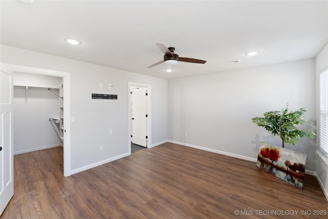 unfurnished bedroom with dark wood-style floors, a spacious closet, recessed lighting, and baseboards