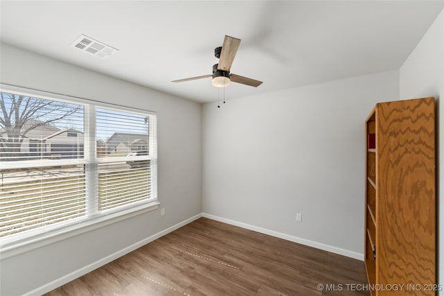 spare room with a ceiling fan, visible vents, baseboards, and wood finished floors