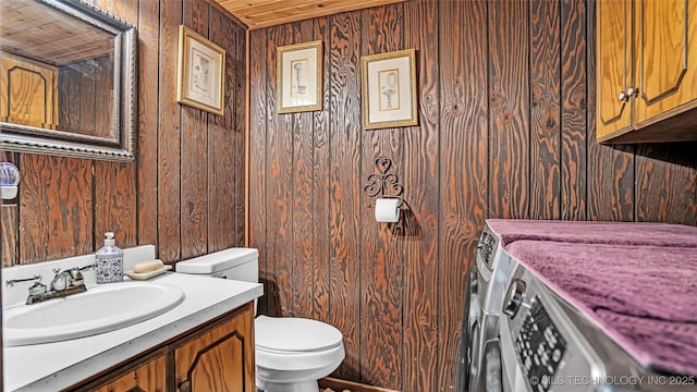 half bathroom featuring vanity, wood walls, washing machine and clothes dryer, and toilet