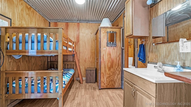 bedroom with wooden walls, a sink, and light wood-style floors