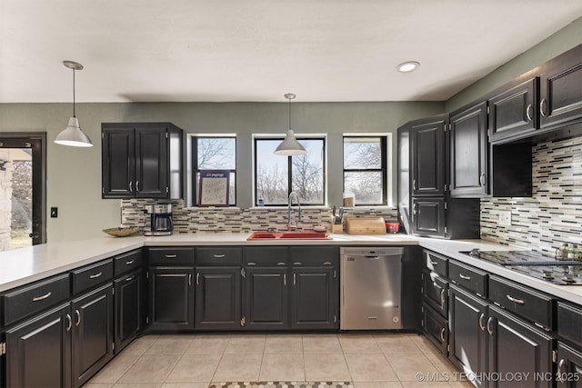 kitchen with stainless steel dishwasher, decorative backsplash, light countertops, dark cabinetry, and a sink