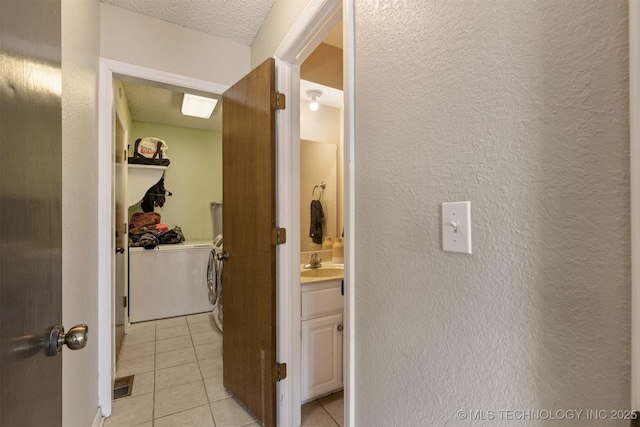 corridor featuring light tile patterned floors, a textured wall, and washer and dryer