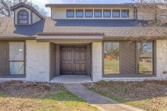 doorway to property featuring stone siding and a shingled roof