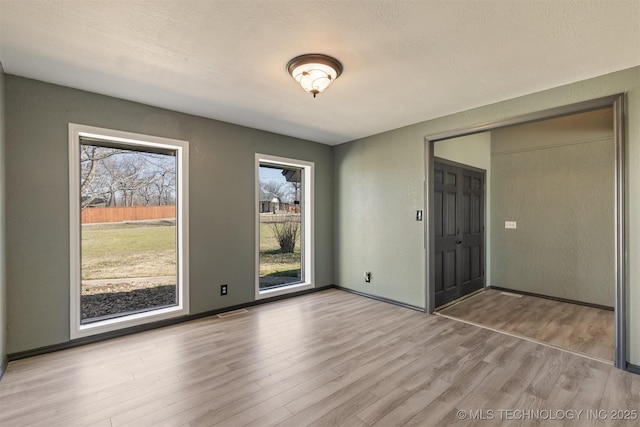 interior space with a textured wall, a textured ceiling, baseboards, wood finished floors, and visible vents