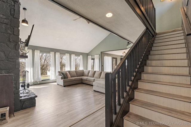 living room with stairs, high vaulted ceiling, wood finished floors, and a fireplace