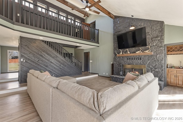 living room with ceiling fan, a stone fireplace, wood finished floors, high vaulted ceiling, and beamed ceiling