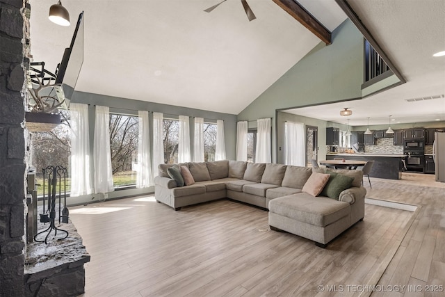living area featuring beam ceiling, light wood finished floors, high vaulted ceiling, a ceiling fan, and visible vents