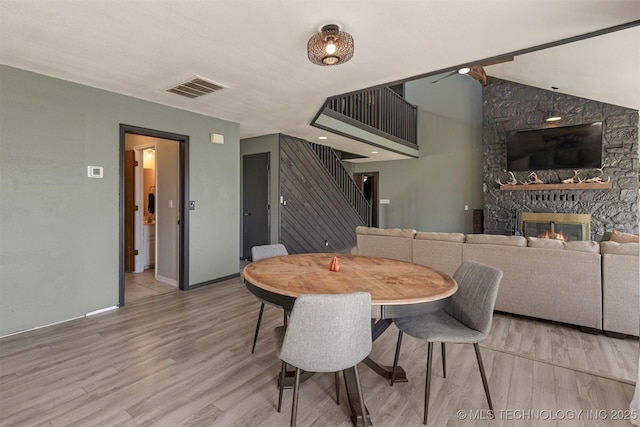 dining space with visible vents, stairs, wood finished floors, baseboards, and a stone fireplace