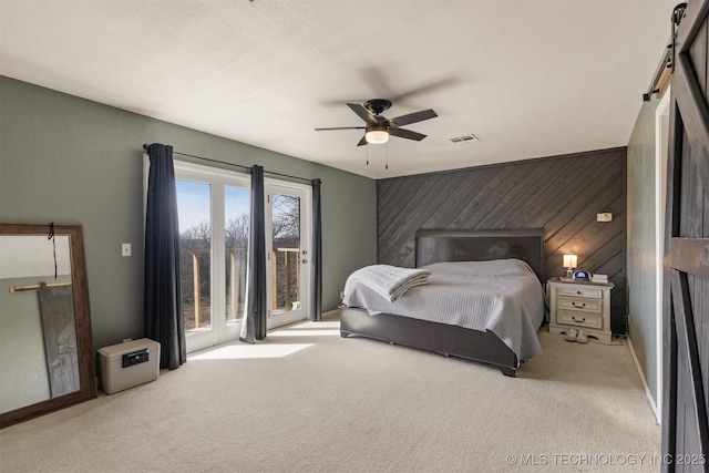 carpeted bedroom with visible vents, access to exterior, wood walls, a barn door, and an accent wall