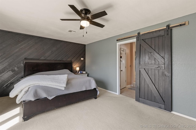 carpeted bedroom with ceiling fan, visible vents, wood walls, a barn door, and baseboards