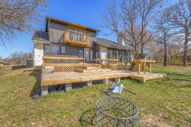rear view of property featuring a lawn, stone siding, a balcony, and a deck