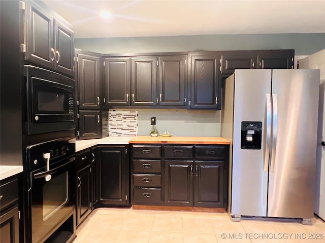 kitchen featuring dark cabinetry, light countertops, light tile patterned flooring, and black appliances