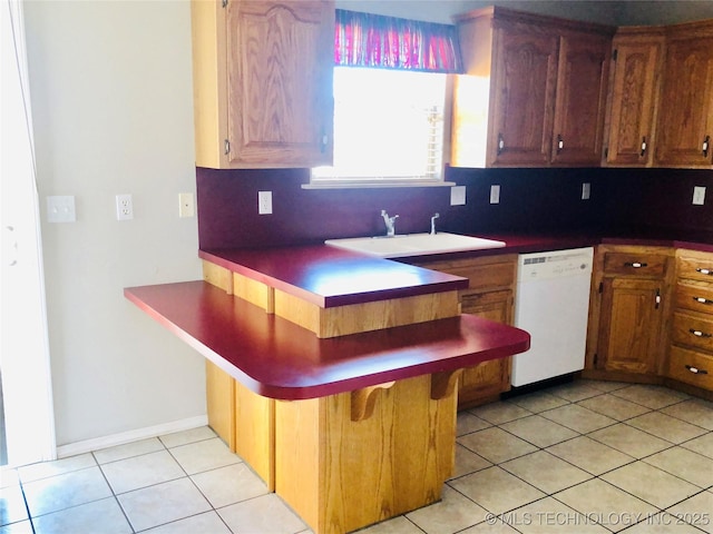 kitchen with light tile patterned floors, a sink, backsplash, dishwasher, and a kitchen bar