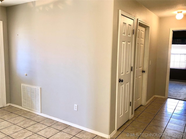 hall with baseboards, visible vents, and light tile patterned flooring