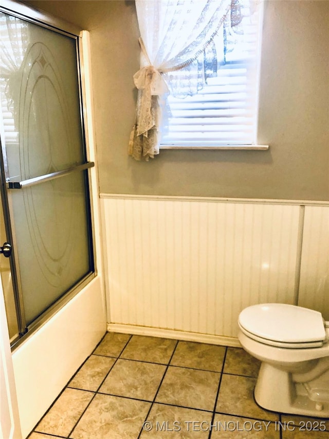 full bath with shower / bath combination with glass door, wainscoting, toilet, and tile patterned floors