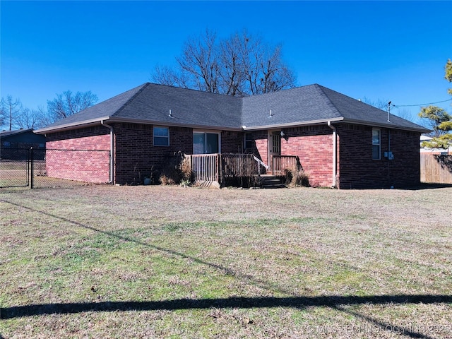 back of house with a yard, brick siding, a shingled roof, and fence