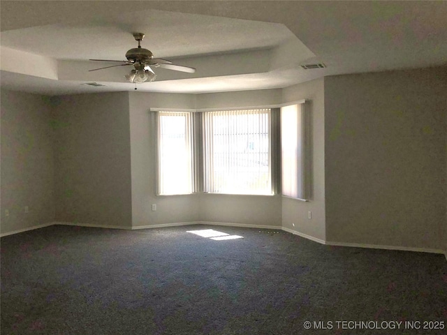 carpeted spare room with a tray ceiling, visible vents, ceiling fan, and baseboards