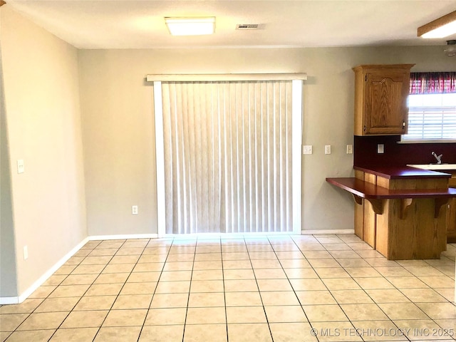 kitchen featuring light tile patterned flooring, a sink, visible vents, and baseboards