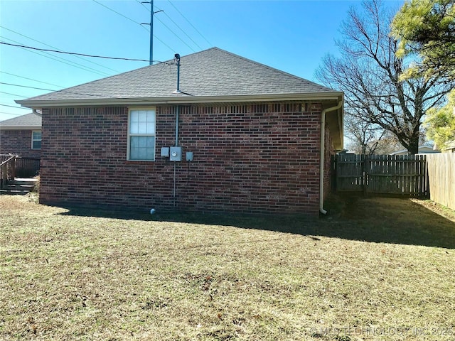 view of side of home with a yard, brick siding, a shingled roof, and fence