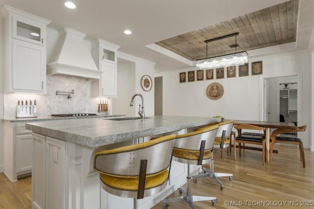 kitchen with a sink, wood ceiling, decorative backsplash, a tray ceiling, and custom range hood