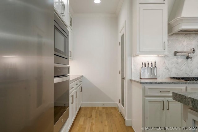 kitchen with white cabinets, ornamental molding, appliances with stainless steel finishes, custom exhaust hood, and tasteful backsplash