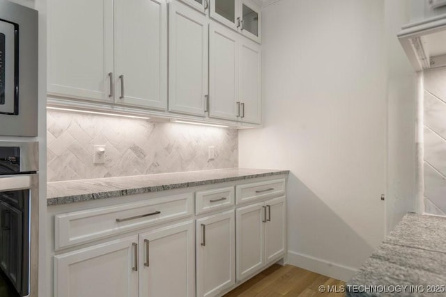 kitchen featuring light stone counters, light wood finished floors, stainless steel appliances, backsplash, and white cabinetry