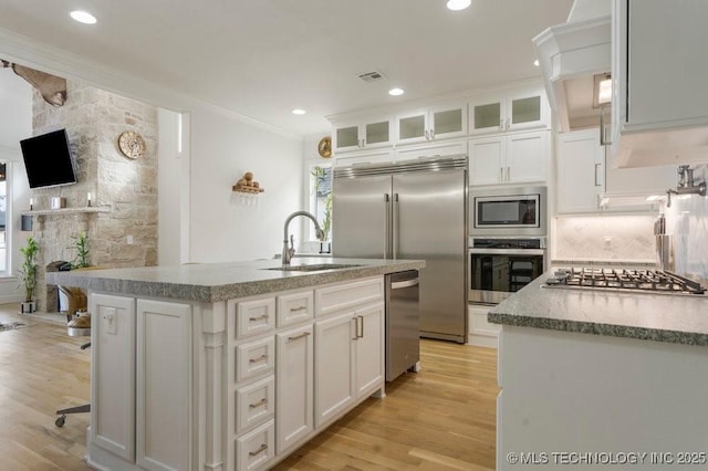 kitchen with built in appliances, a sink, white cabinets, ornamental molding, and light wood finished floors