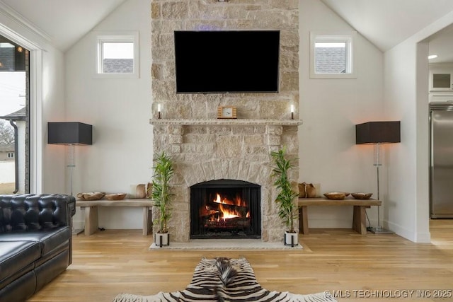 living room featuring lofted ceiling, a stone fireplace, and wood finished floors