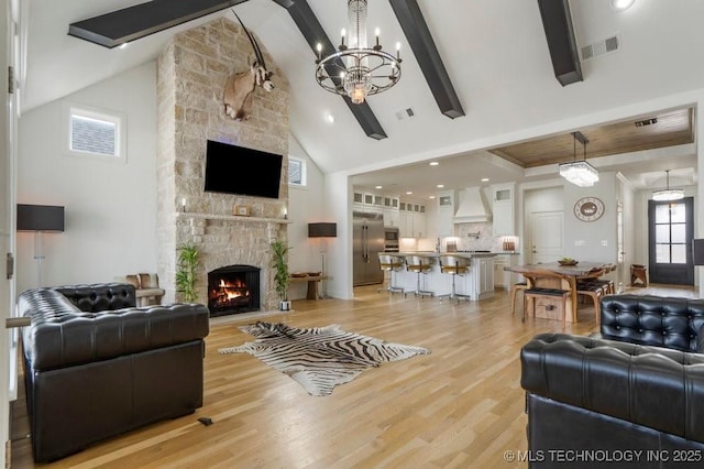 living room with light wood-type flooring, visible vents, beamed ceiling, and a stone fireplace