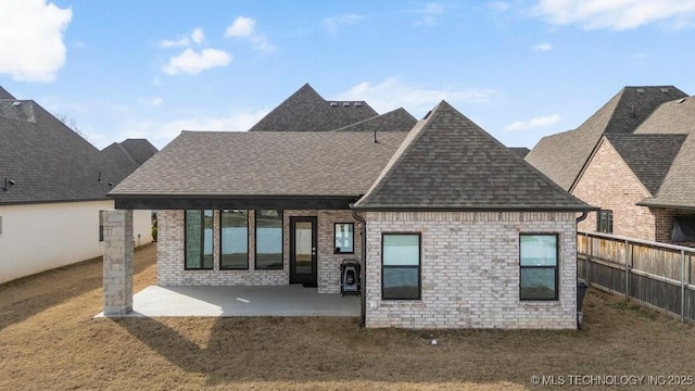 back of house featuring a patio, a shingled roof, brick siding, fence, and a lawn