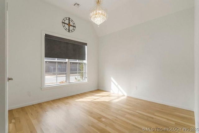 spare room with lofted ceiling, a chandelier, wood finished floors, visible vents, and baseboards