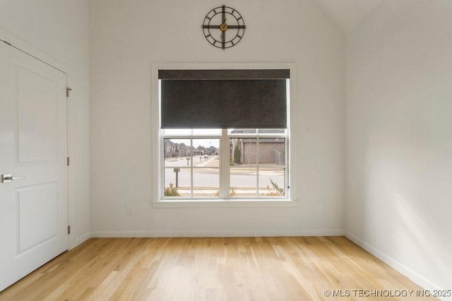 spare room featuring light wood-type flooring, baseboards, and lofted ceiling