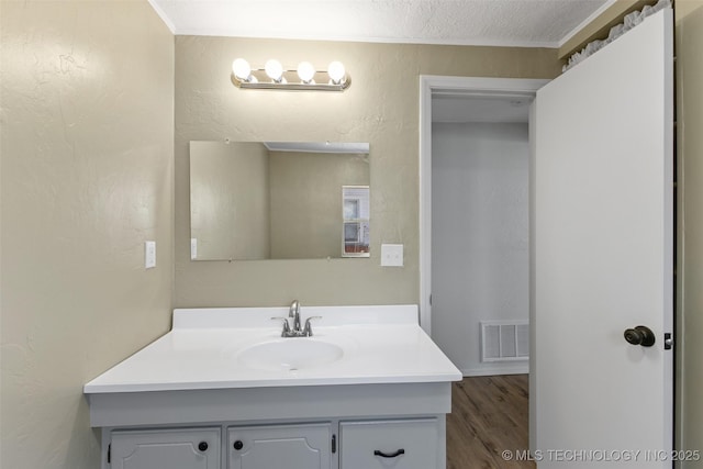 bathroom with a textured ceiling, a textured wall, wood finished floors, vanity, and visible vents